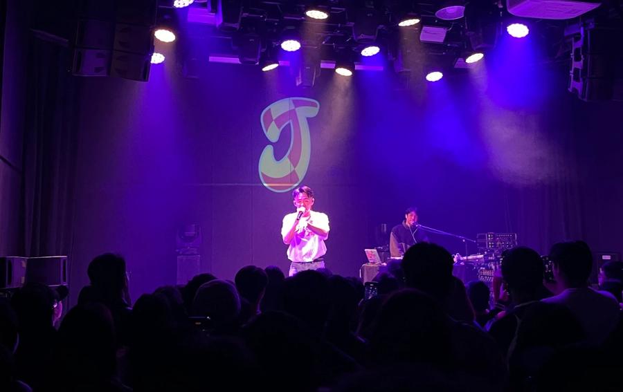 rapper with microphone in front of giant J, next to him is a DJ