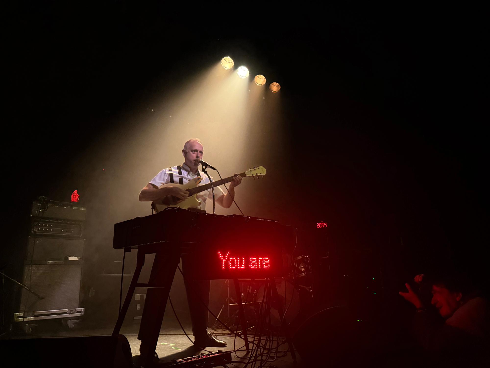 Litronix on guitar singing in mic; and LED screen shows 'you are' in red letters