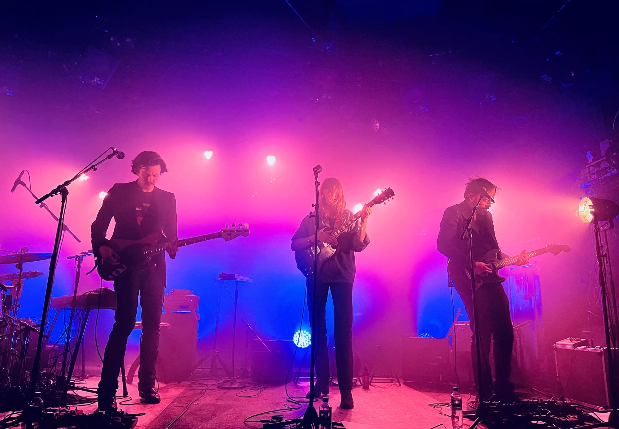 Roos playing tuirar in the middle, two guitars left and right (one probably bass), the light in the back is partially pink, partially blue