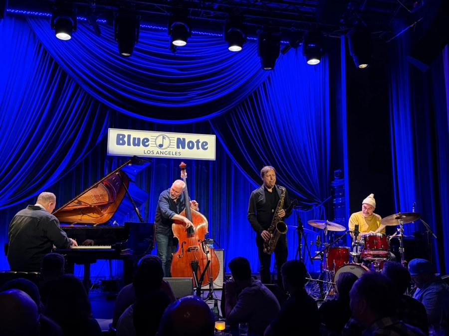 Craig Taborn, Reid Anderson, Chris Potter and Dave King on stage playing grand piano, double bass, saxophone and drums, in the back is a blue curtain and a blue note los angeles sign