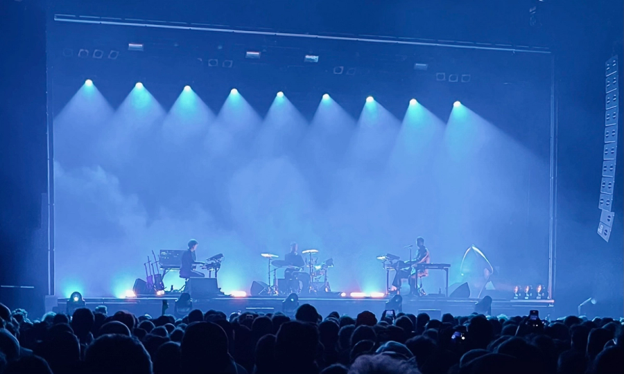 three musicians on stage, from left to right keyboard, drums and James Blake, also behind keyboard