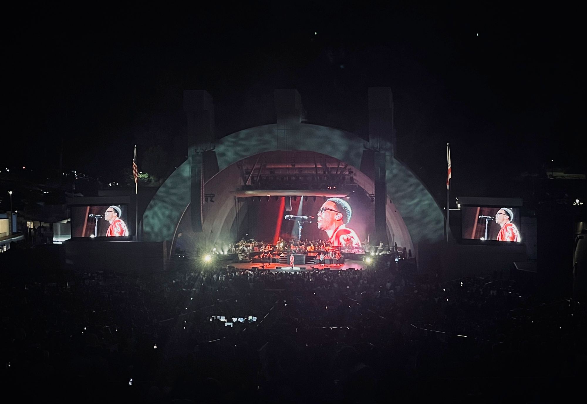 anderson paak playing seen from a distance, his face is on three screens, one behind the stage and one on either side