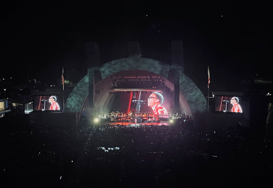 anderson paak playing seen from a distance, his face is on three screens, one behind the stage and one on either side