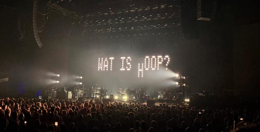 band playing, behind them are LCD letters that say “wat is hoop?”