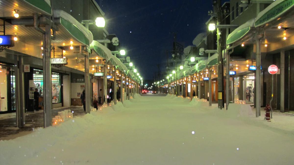 雪夜的稚內中央商店街，兩側騎樓亮著燈，路邊排著冰燈