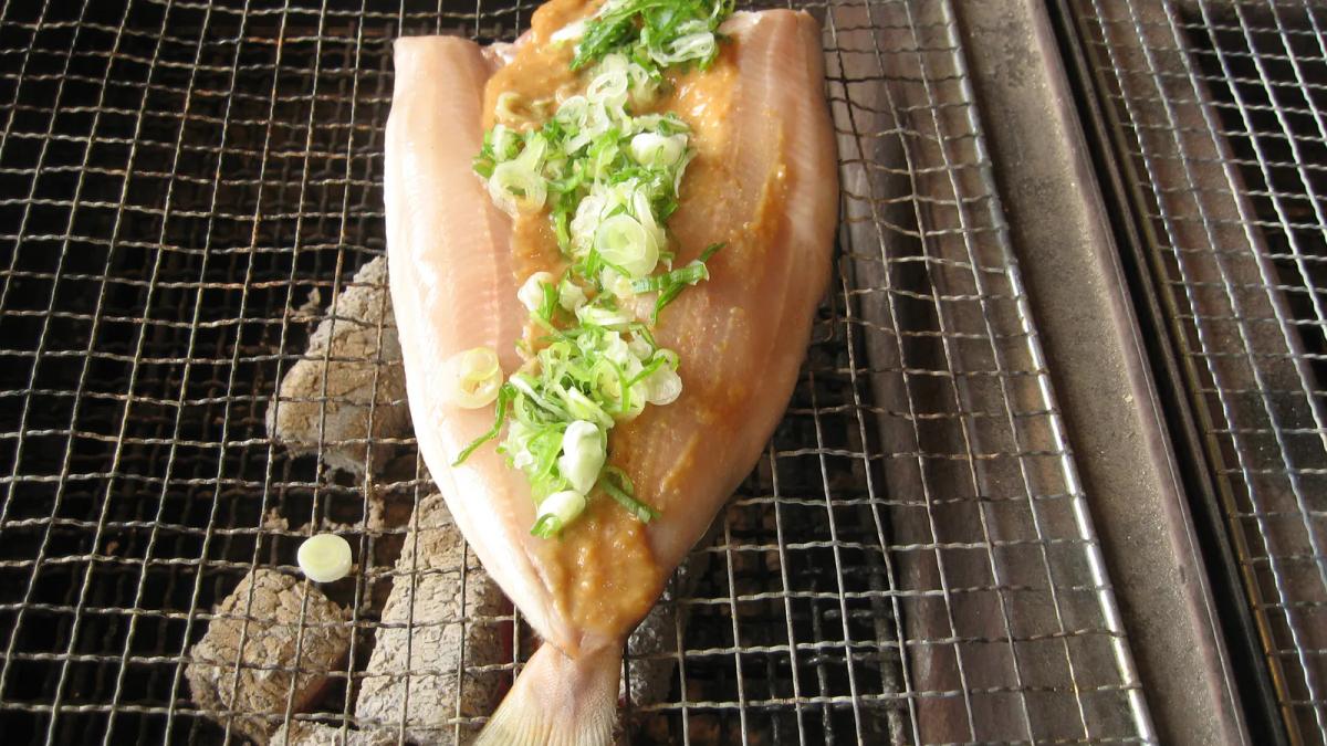 炭火網上整片剖開的花魚，魚身抹了味噌、鋪滿蔥花，正在烤成鏘鏘燒