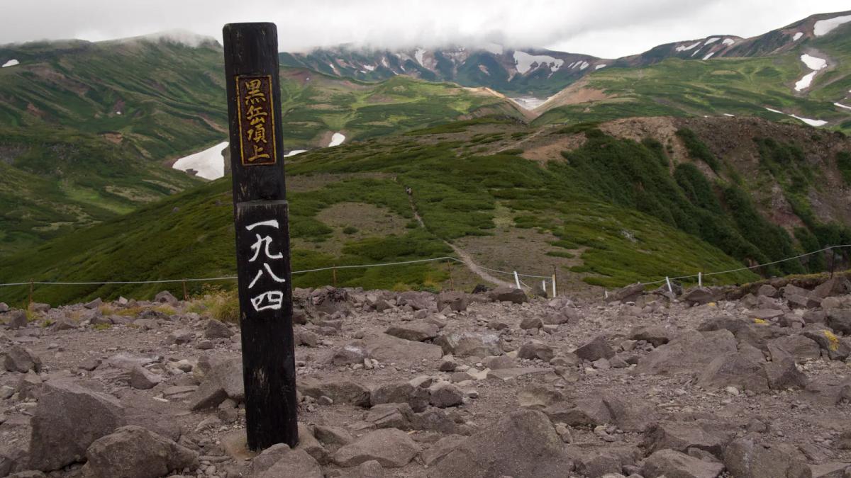黑岳山頂的木製標柱，寫著黒岳頂上與標高一九八四，背後是夏天殘雪點點的大雪山群