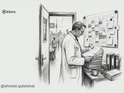 From behind, an international doctor sits at a kitchen table with a German hospital application open on a laptop, a CV page, licence copy, and a handwritten Dienstplan pinned beside a window showing a