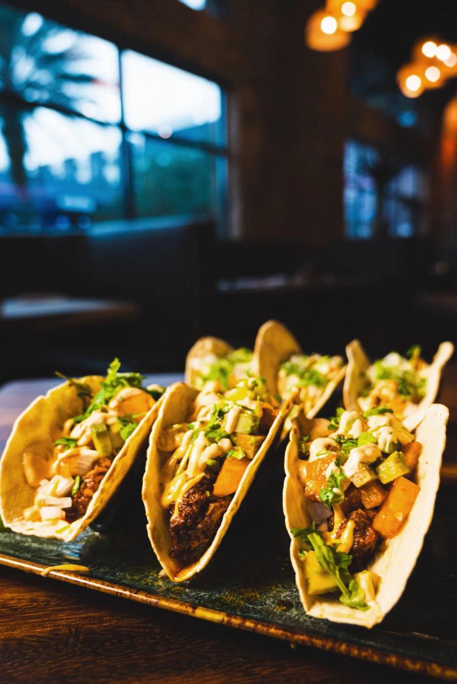 Three street tacos with cilantro and onion on a board at Cantina Añejo
