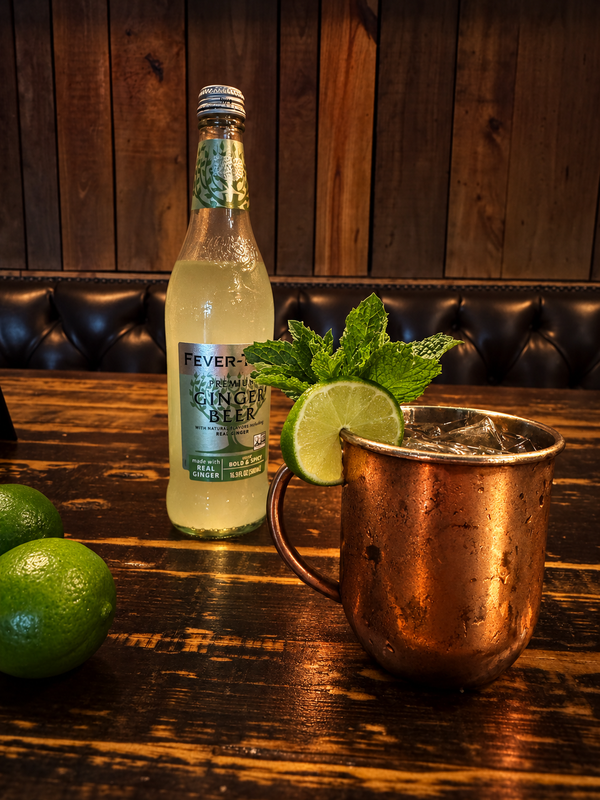 A copper mule mug with lime and mint beside a ginger beer bottle