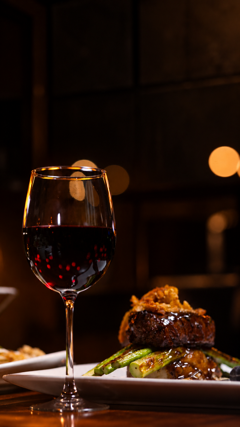A glass of red wine beside the filet on a dark wood table