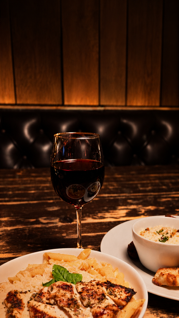 Red wine with chicken pasta at a leather banquette