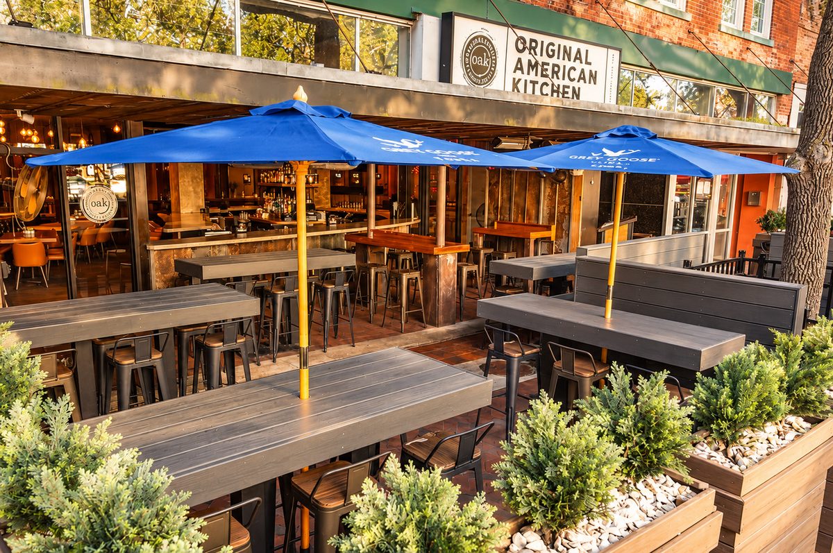 OAK's patio on SE 1st Ave under blue umbrellas, looking into the bar beneath the Original American Kitchen sign