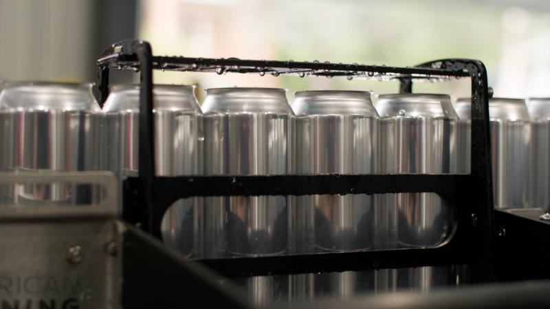 Rows of unlabeled aluminum cans fresh from the canning line, wet with condensation and held in a metal carrier rack.