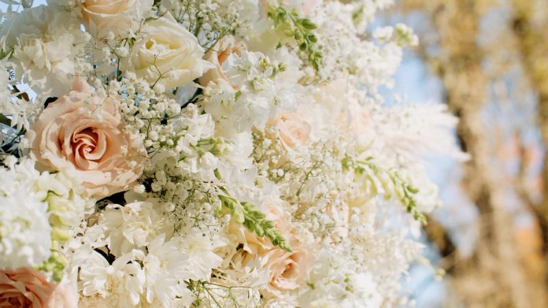 A close-up of a lush wedding floral arrangement featuring blush and white roses, baby's breath, and delicate white blooms against a soft bokeh background.
