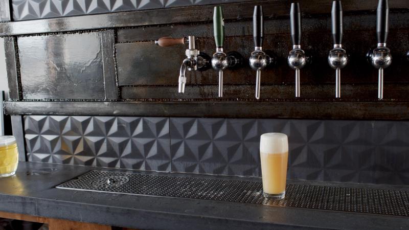 A freshly poured hazy IPA in a pint glass sits on the bar at Old Thunder Brewing Company, with industrial tap handles and textured tile visible in the background.