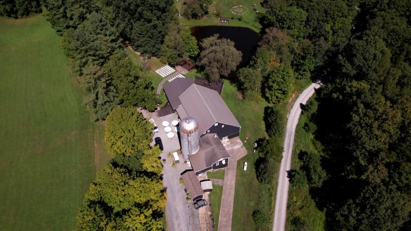 Straight-down aerial drone shot of Chanteclaire Farm in Friendsville, Maryland, showing the barn venue, grain silo, ceremony chairs set up on the lawn, the pond, and surrounding fields and forest.