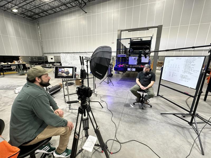 Two-person video production crew filming executive interview in manufacturing facility