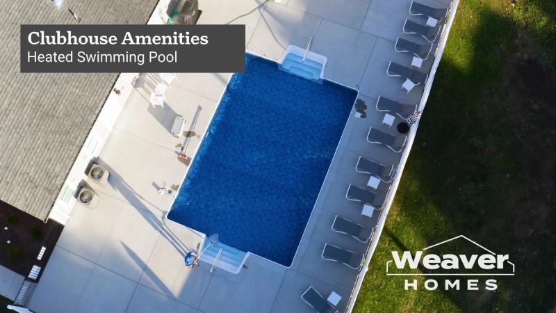 Aerial drone shot looking straight down at the Heritage Crossings clubhouse heated pool, with the on-screen graphic overlay reading "Clubhouse Amenities: Heated Swimming Pool" and the Weaver Homes logo.