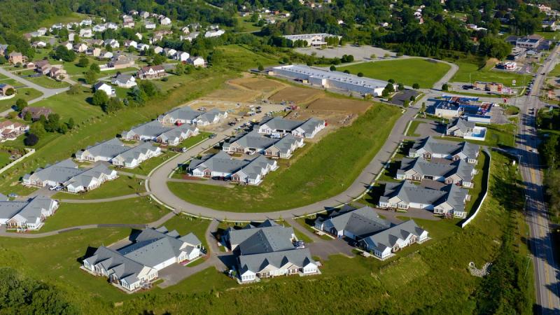 High aerial drone shot looking down at the full Heritage Crossings development, showing the layout of completed and under-construction Weaver Homes across a curved road network.
