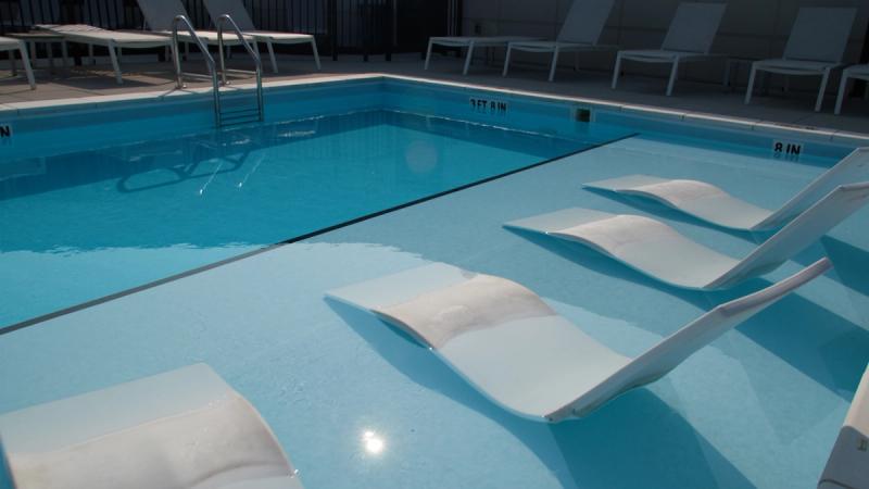 A rooftop pool at Brewer's Block apartments in Pittsburgh, with white in-water lounge chairs partially submerged along the shallow end and additional lounge chairs arranged along the pool deck.