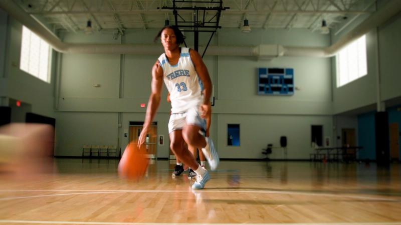 Freire Charter School student in basketball uniform dribbling on an indoor court during admissions video production