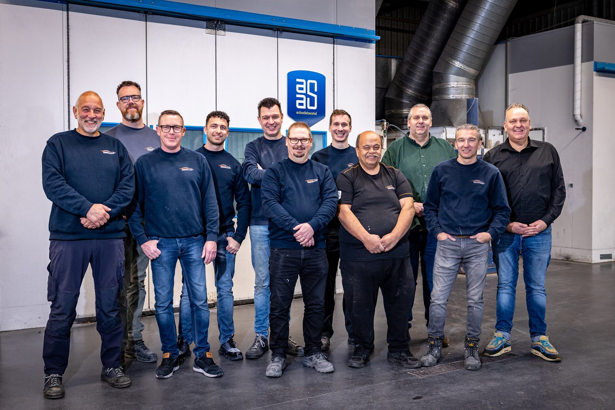 Het voltallige team van Autoschade Merkelbag poseert samen in de werkplaats in Maastricht