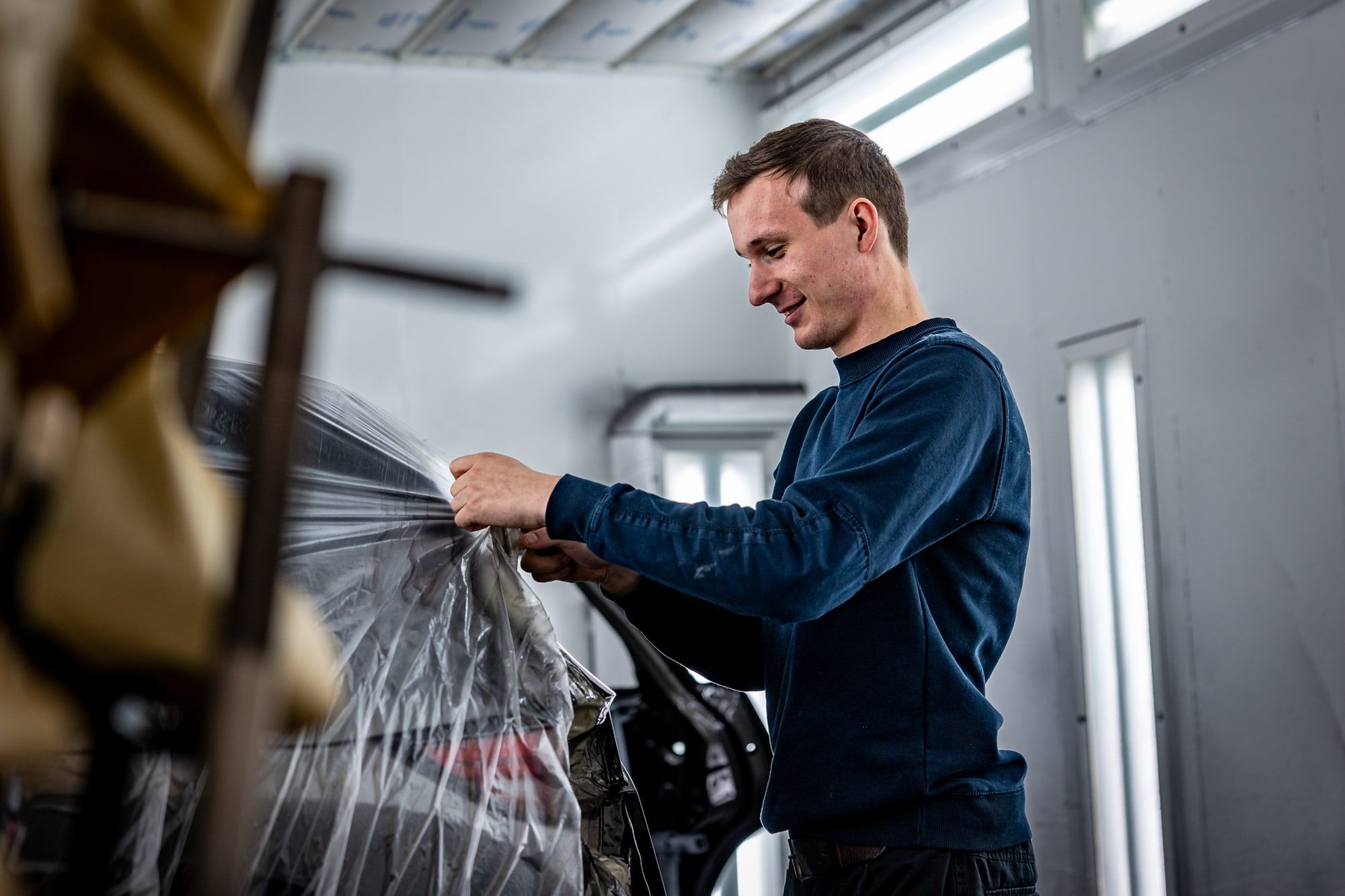 Medewerker van Autoschade Merkelbag plakt een portier af met beschermfolie in de spuitcabine, ter voorbereiding op spuitwerk