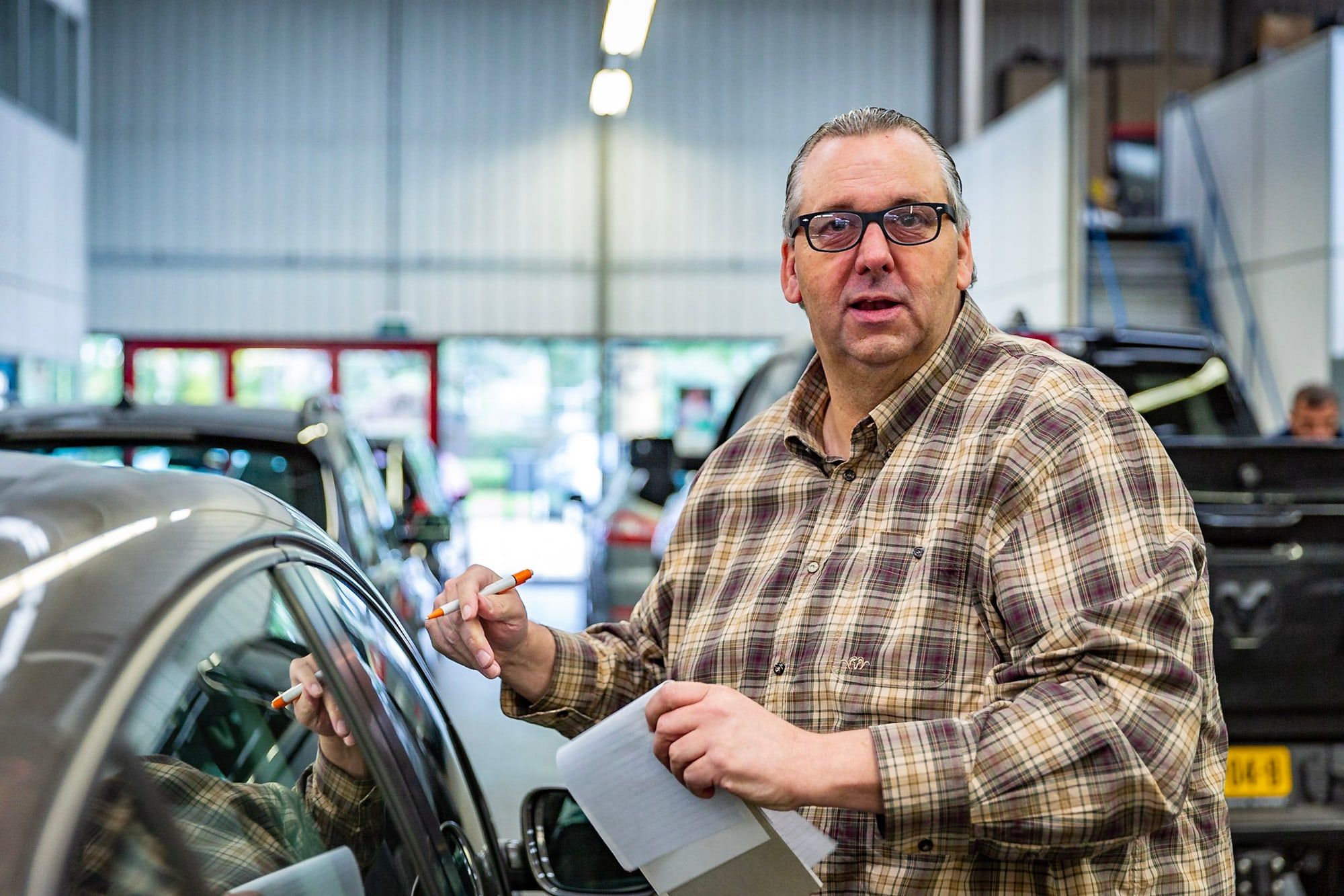 Schade-expert beoordeelt met klembord en pen de schade aan een auto in de werkplaats van Autoschade Merkelbag