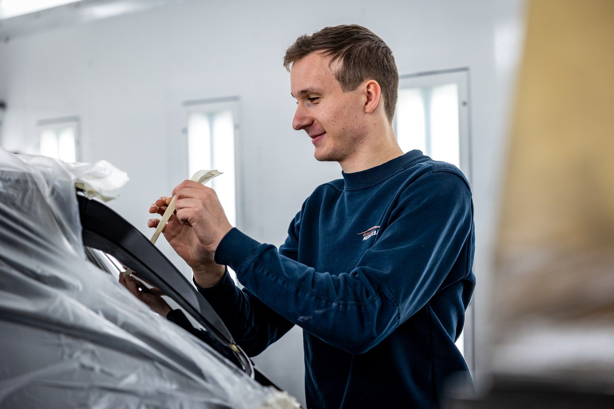 Medewerker van Autoschade Merkelbag plakt een auto zorgvuldig af in de spuitcabine voor het lakwerk