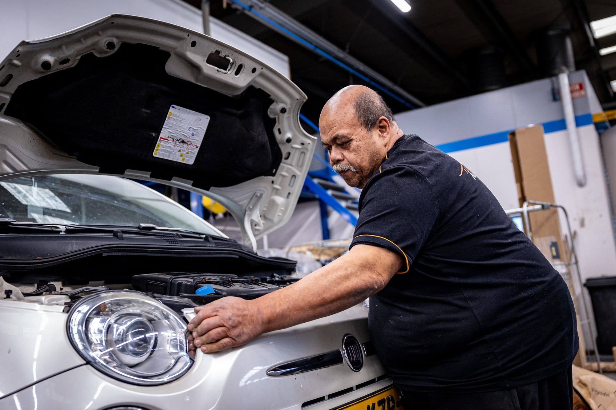 Monteur van Autoschade Merkelbag werkt onder de open motorkap van een auto in de werkplaats