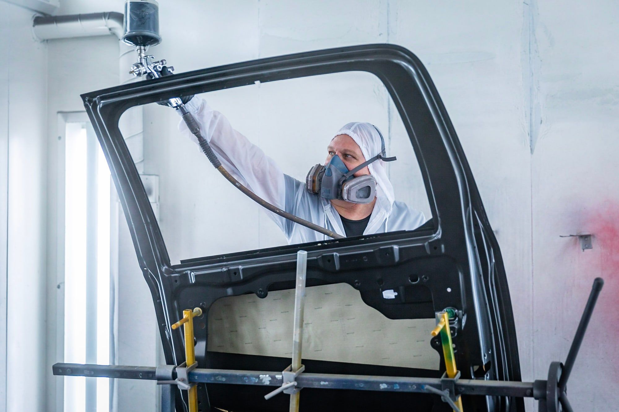 Spuiter van Autoschade Merkelbag lakt een portier in de spuitcabine tijdens schadeherstel