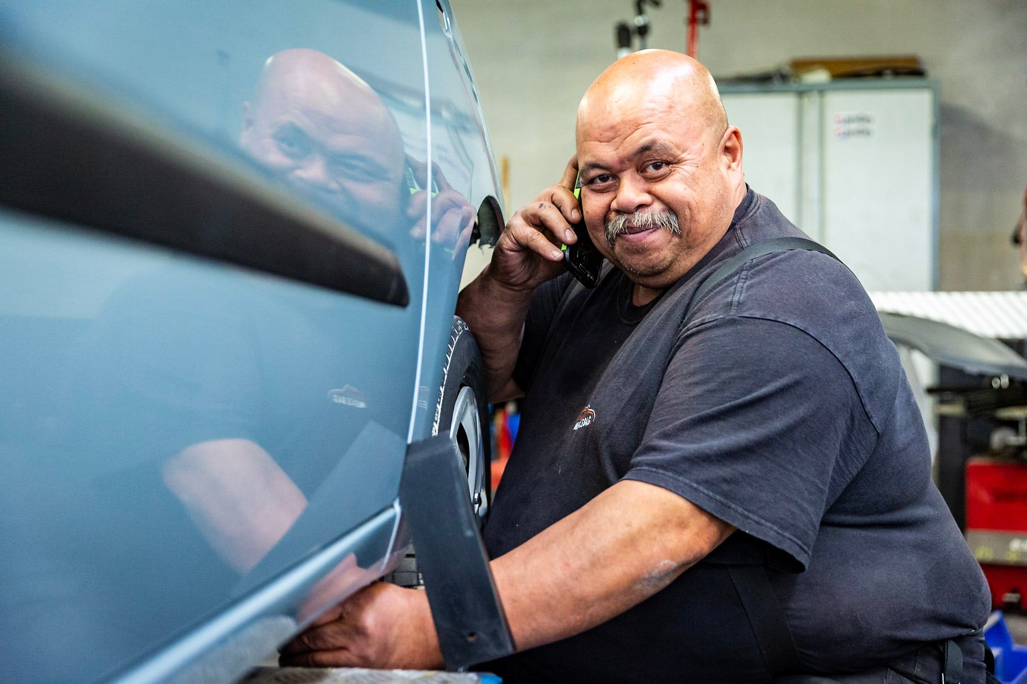 Medewerker van Autoschade Merkelbag staat een klant telefonisch te woord bij een auto in de werkplaats in Maastricht