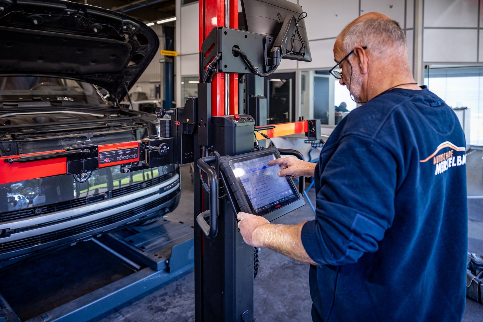 Monteur van Autoschade Merkelbag leest met een diagnosetablet een moderne auto uit bij de kalibratieopstelling in de werkplaats