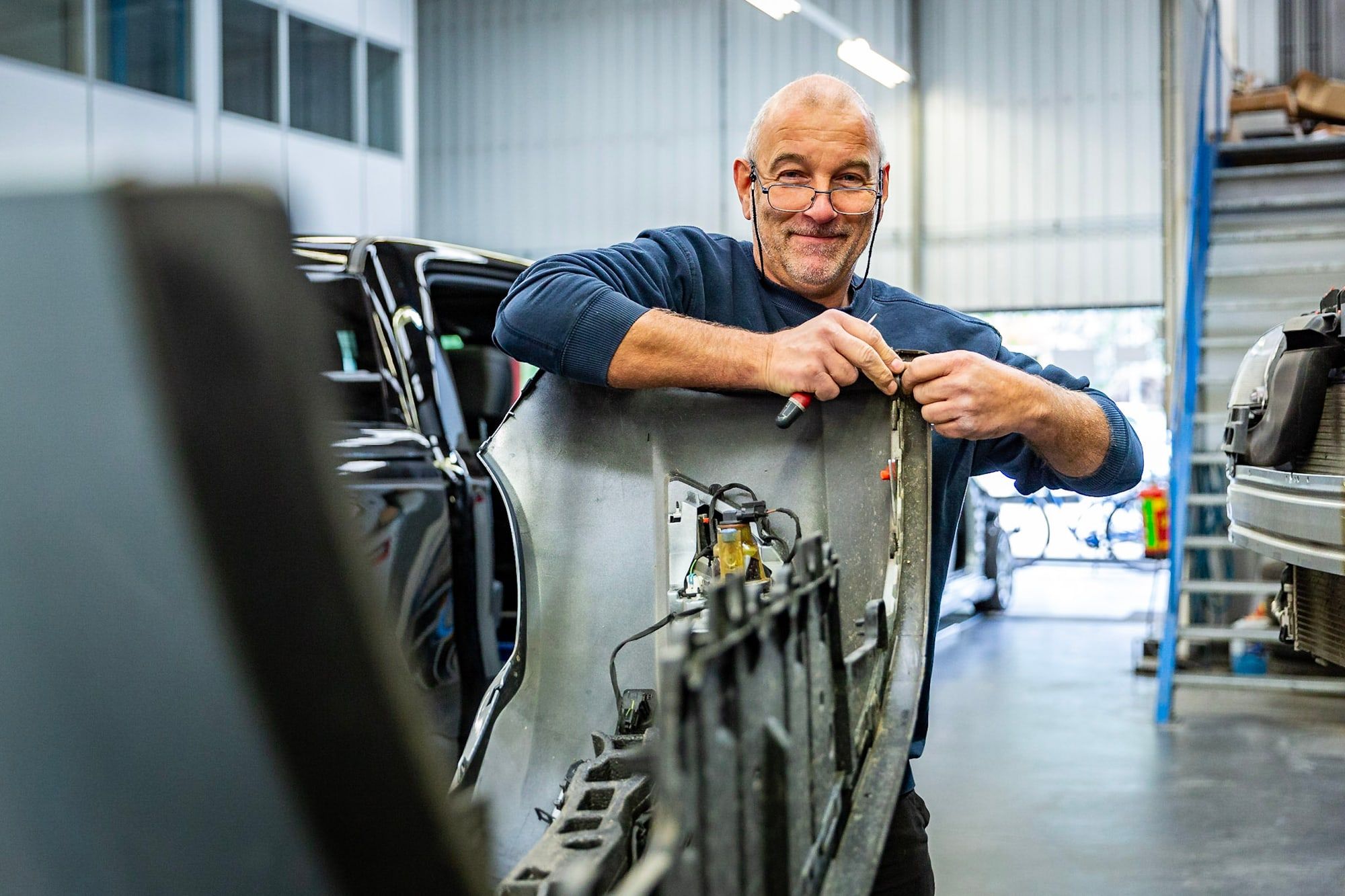 Monteur van Autoschade Merkelbag werkt in de werkplaats aan een auto waarvan de carrosseriedelen zijn gedemonteerd