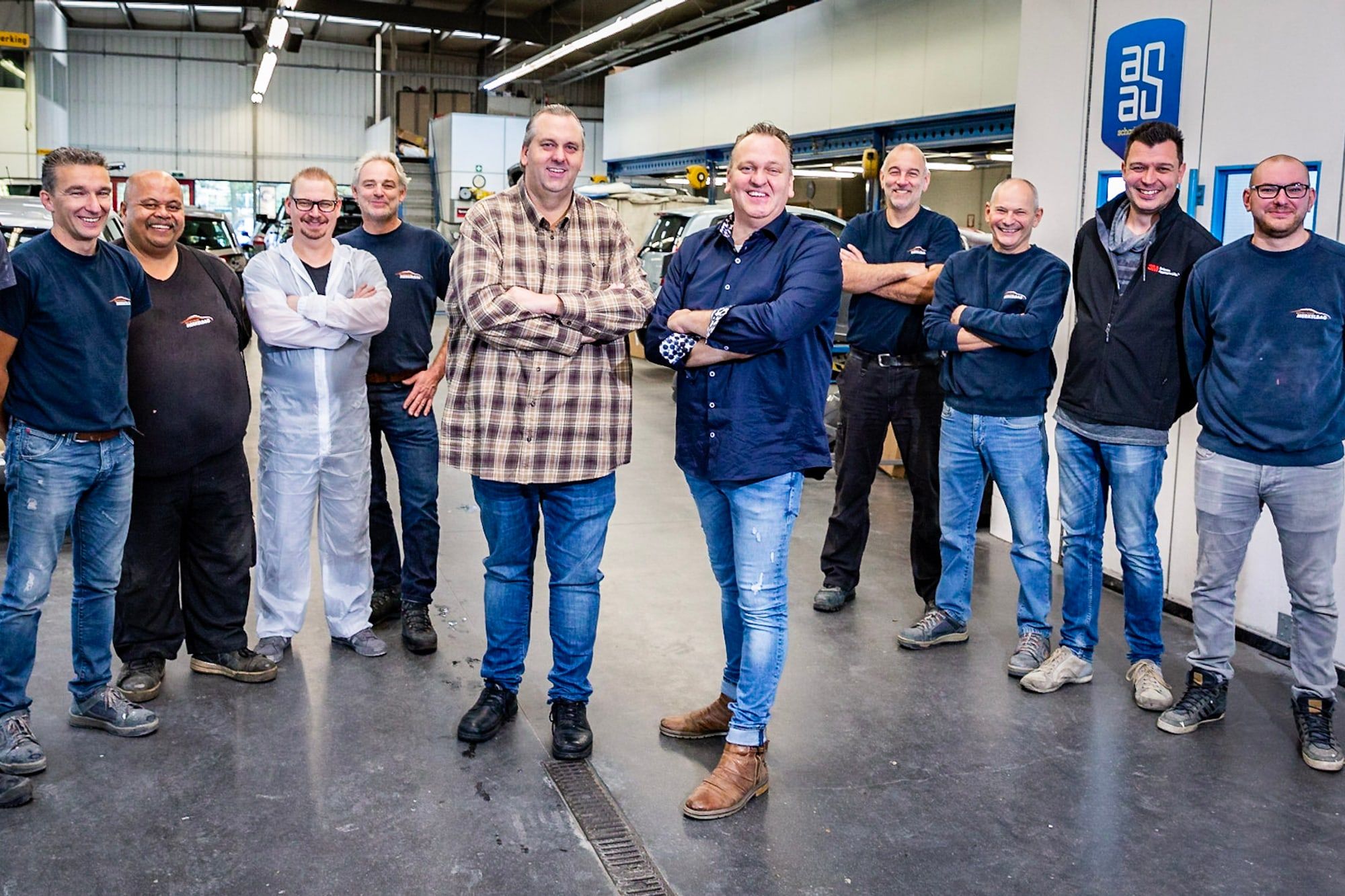 Het team van Autoschade Merkelbag poseert samen in de werkplaats in Maastricht