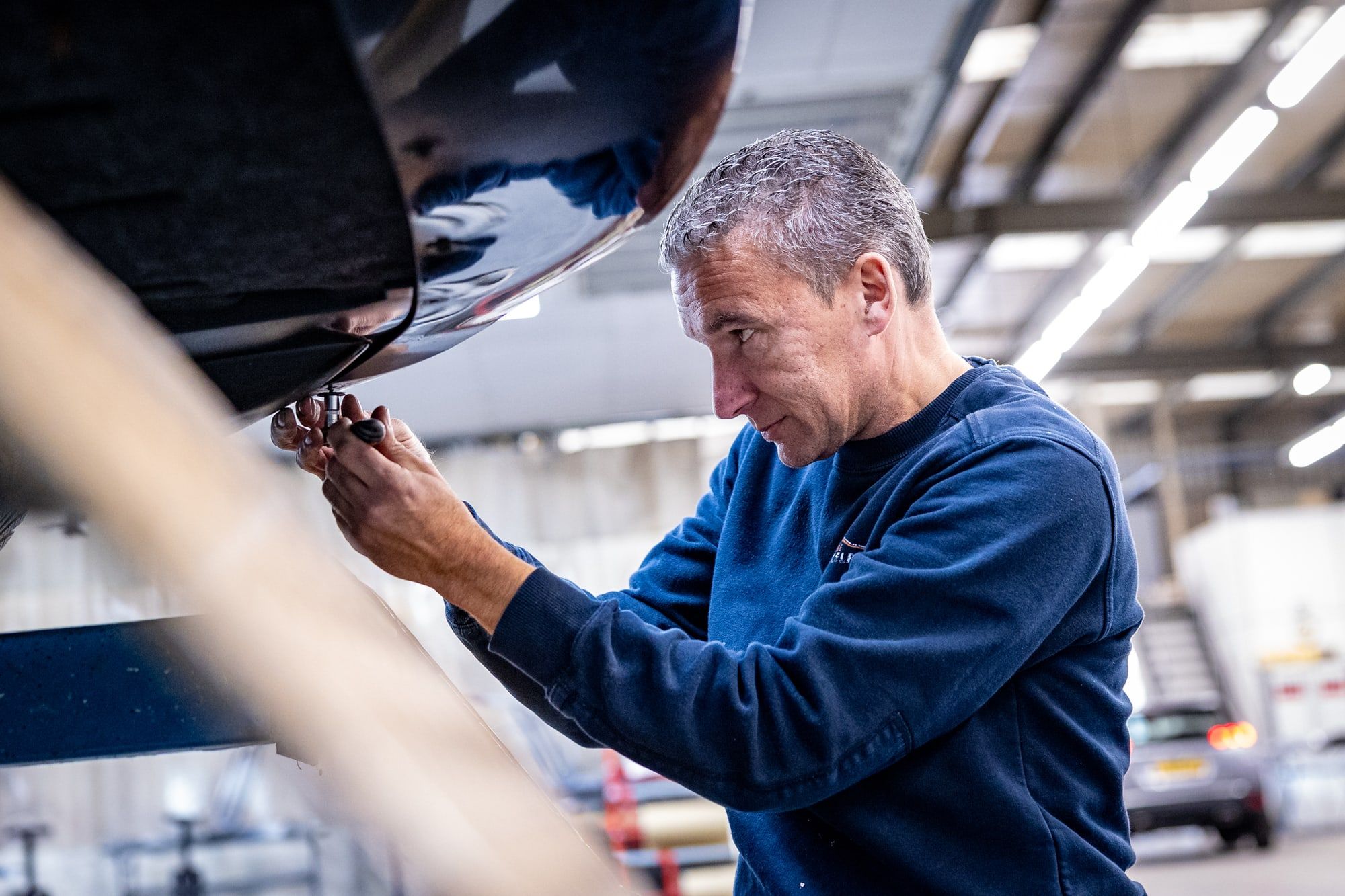 Monteur van Autoschade Merkelbag inspecteert en herstelt het onderstel van een geheven auto, de plek waar roest vaak begint