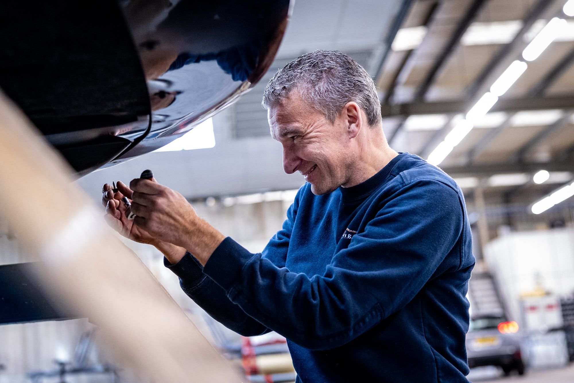 Monteur van Autoschade Merkelbag controleert de wielophanging aan de onderkant van een auto in de werkplaats