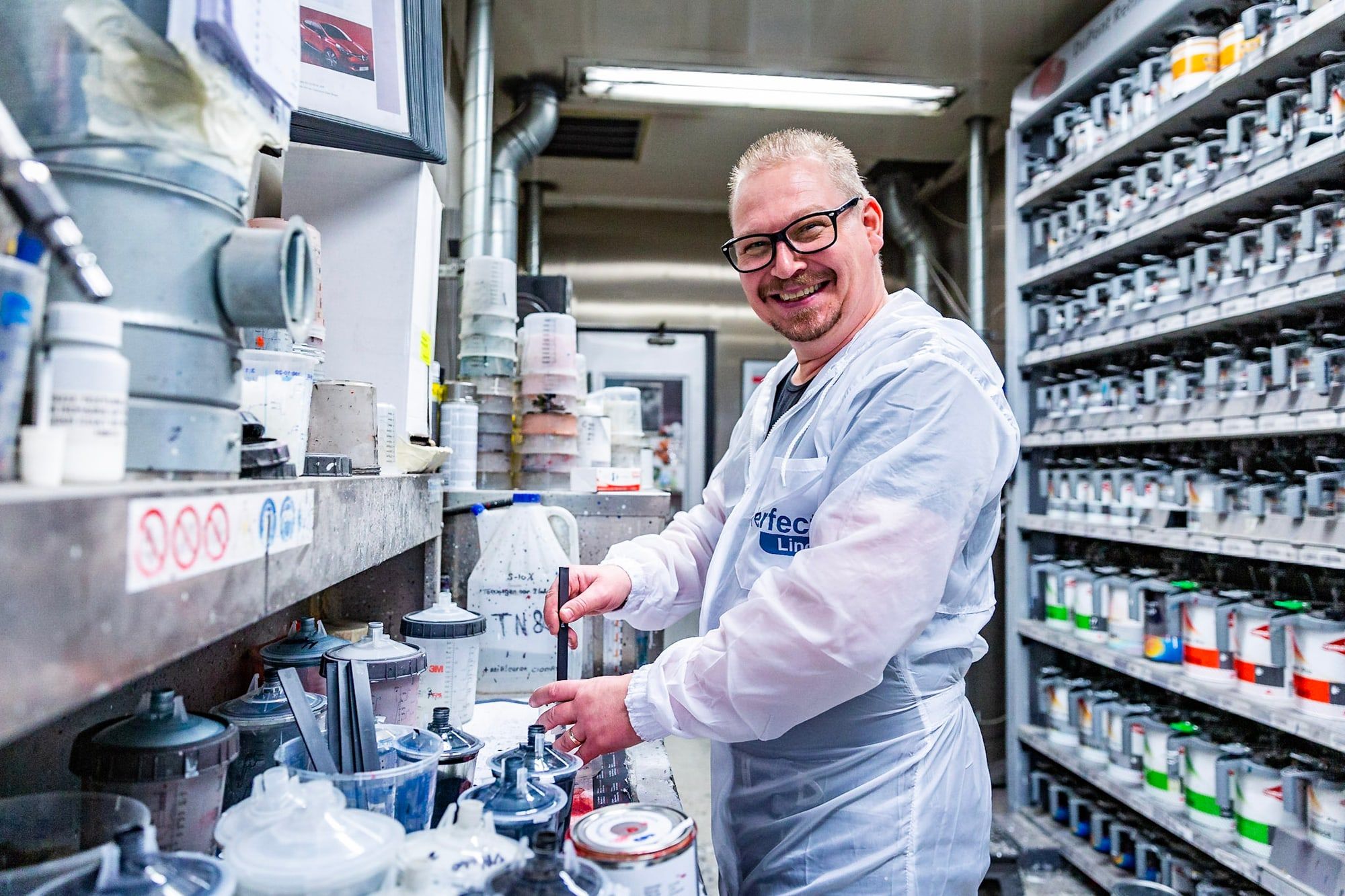 Lakspecialist van Autoschade Merkelbag mengt een verfkleur op maat tussen de rekken met lakblikken