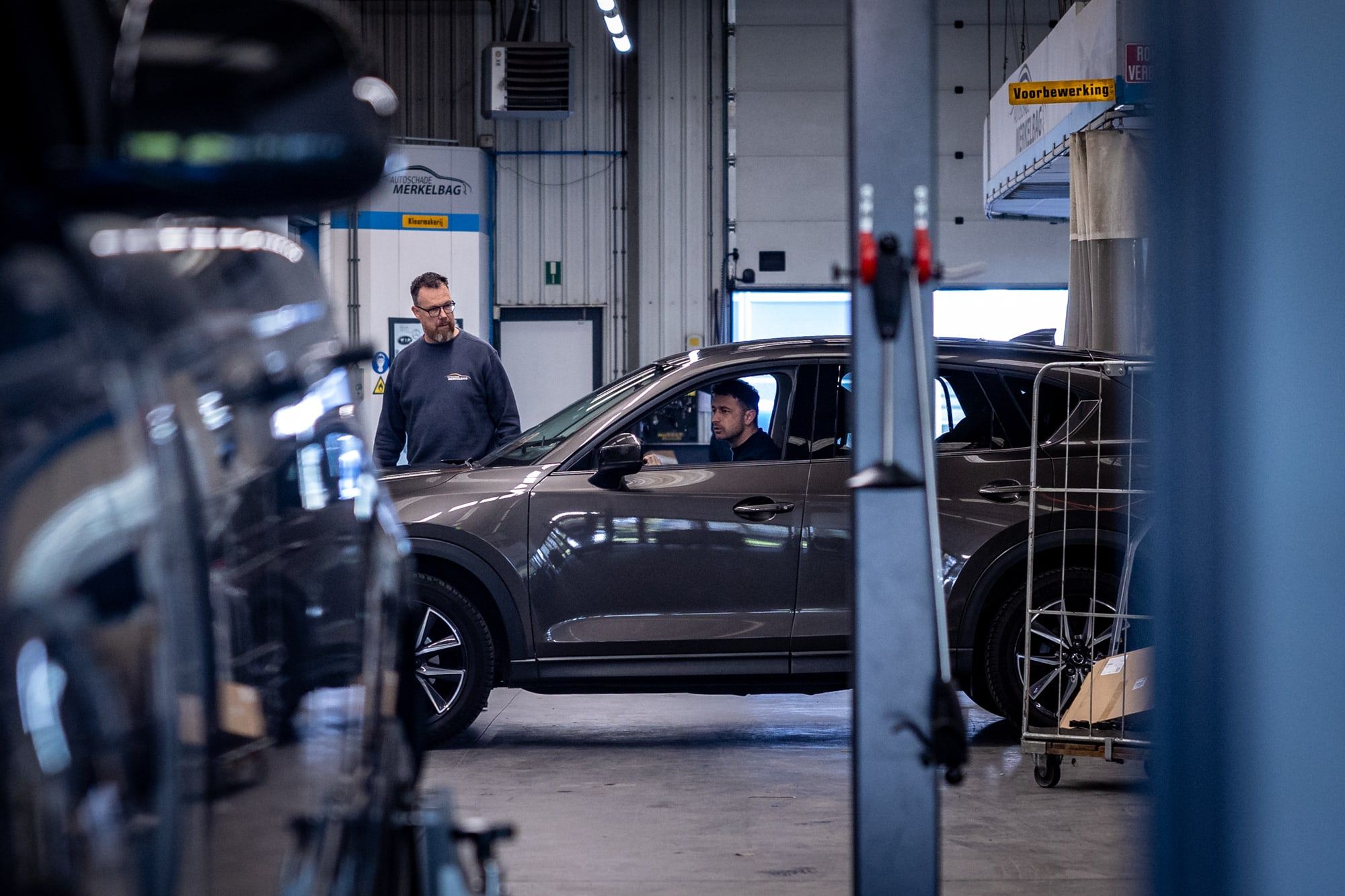 Klant rijdt zijn auto de werkplaats van Autoschade Merkelbag in Maastricht binnen en wordt ontvangen door een medewerker