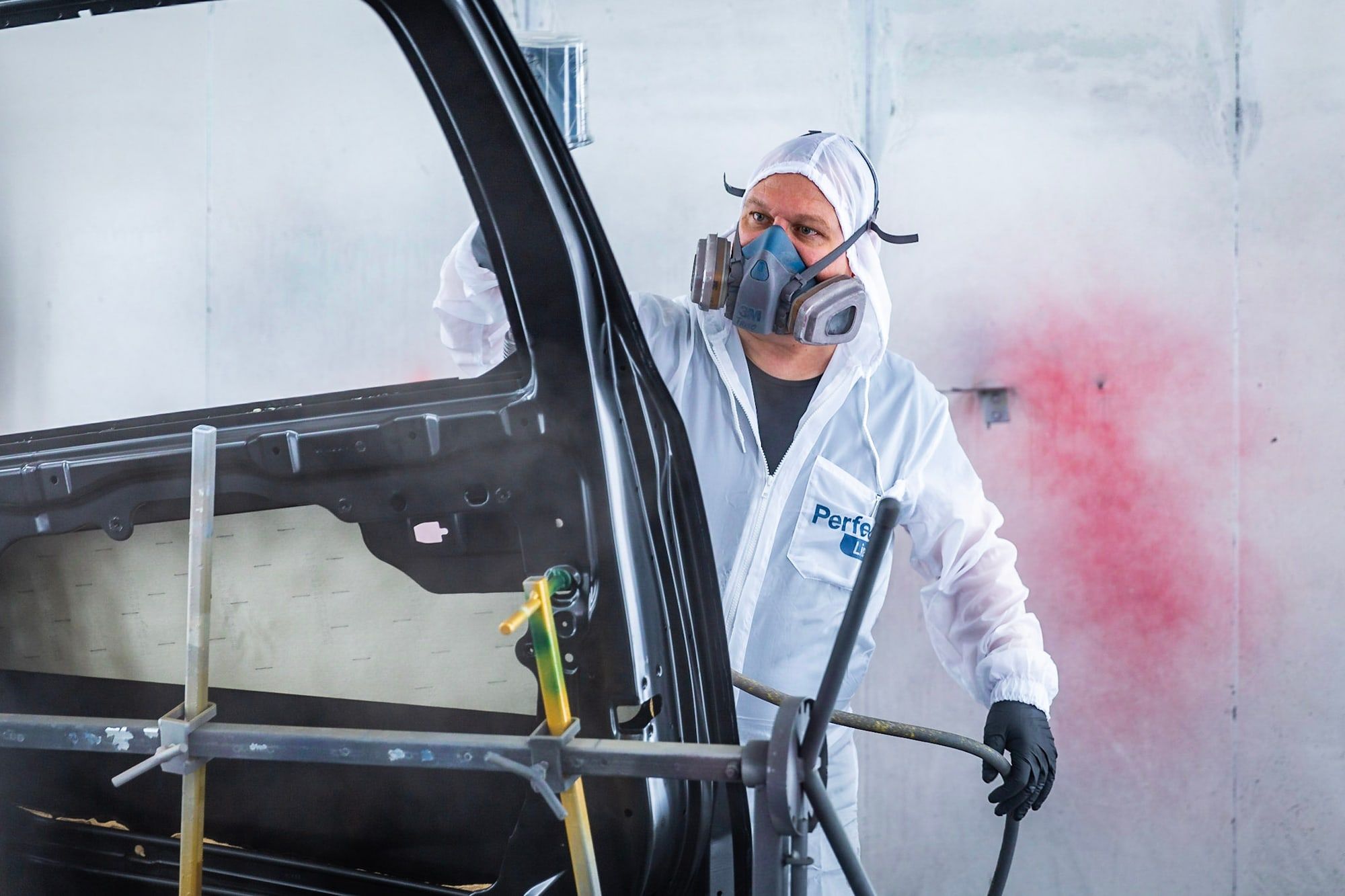 Autospuiter van Autoschade Merkelbag herstelt het lakwerk van een autoportier in de spuitcabine