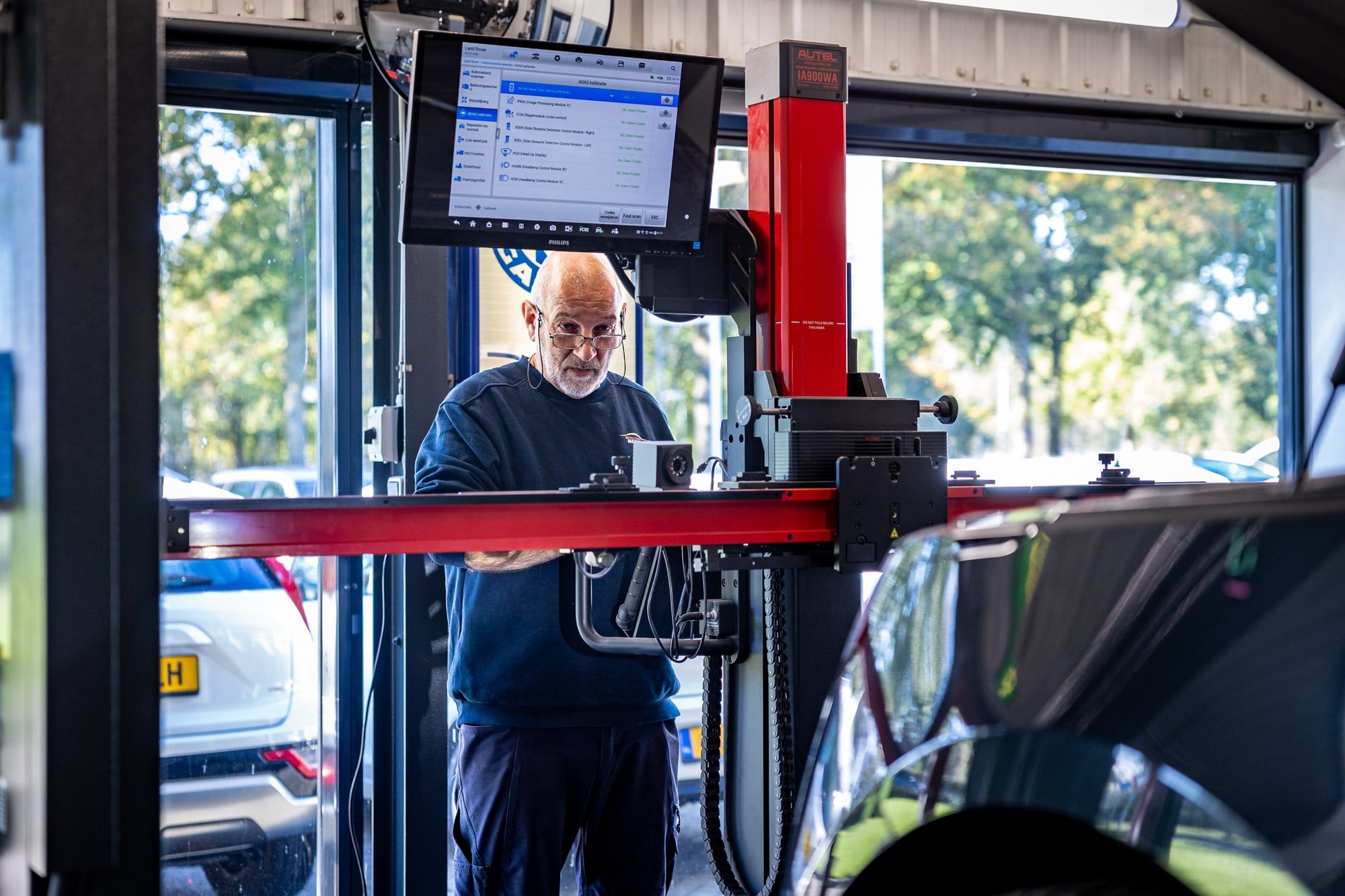 Medewerker in de werkplaats van Autoschade Merkelbag in Maastricht bij een kalibratiesysteem, met op het scherm de elektronische modules van de auto, waaronder de koplampbesturing