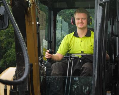 Elev sitter inne i liten gravemaskin, ser i kamera