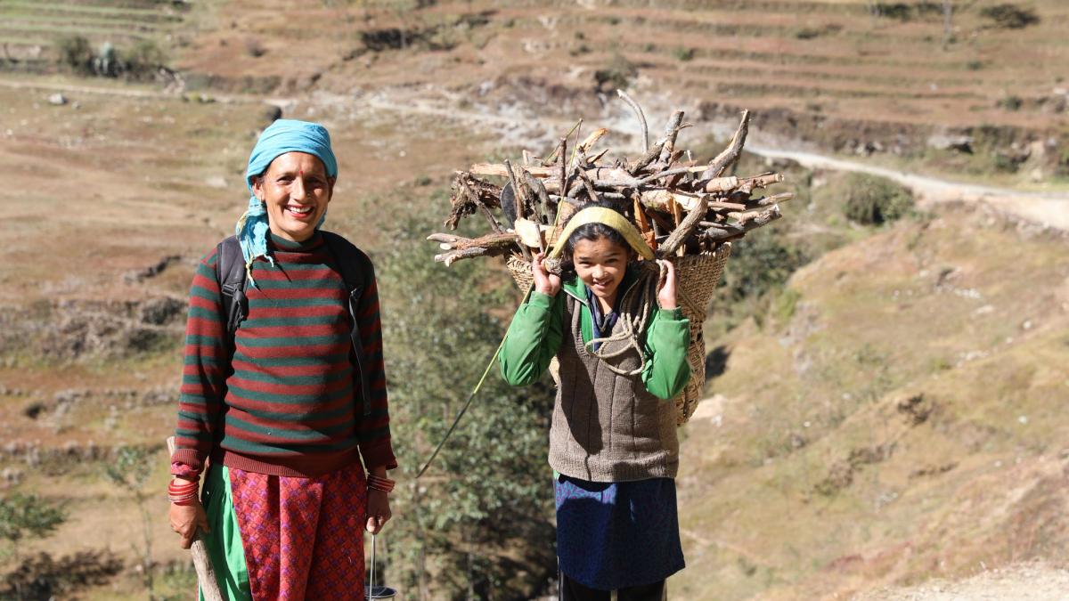 To damer smiler, ung jente med tung last på ryggen
