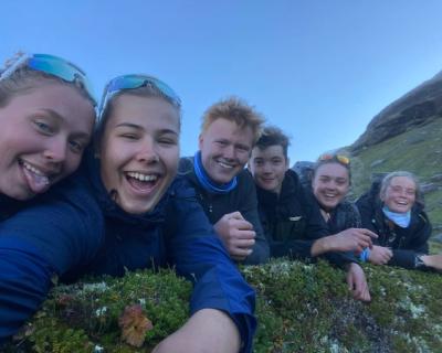 Seks elever som ligger på magen på et fjell, smiler inn i camera