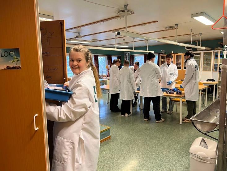 Lærer og elever i hvite lab-frakker i et klasserom.