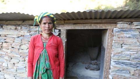 Ei dame foran lita steinhytte med mølle på vannkraft