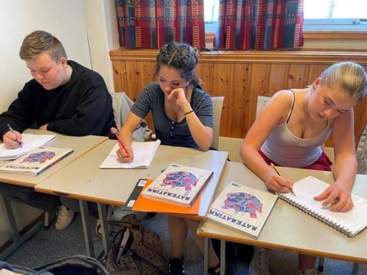 Tre elever sitter bak skolepulten og regner matte med blyant og papir.