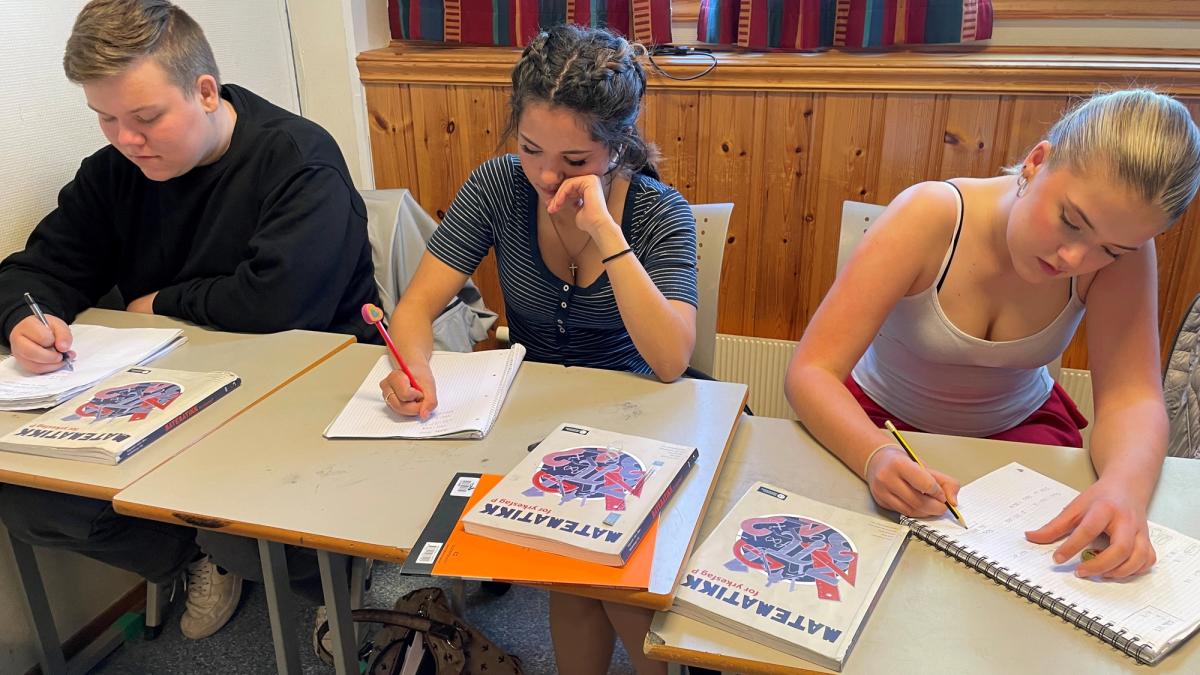 Tre elever sitter bak skolepulten og regner matte med blyant og papir.