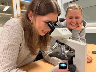 2 elever sitter ved en skolepult og kikker i et mikroskop.